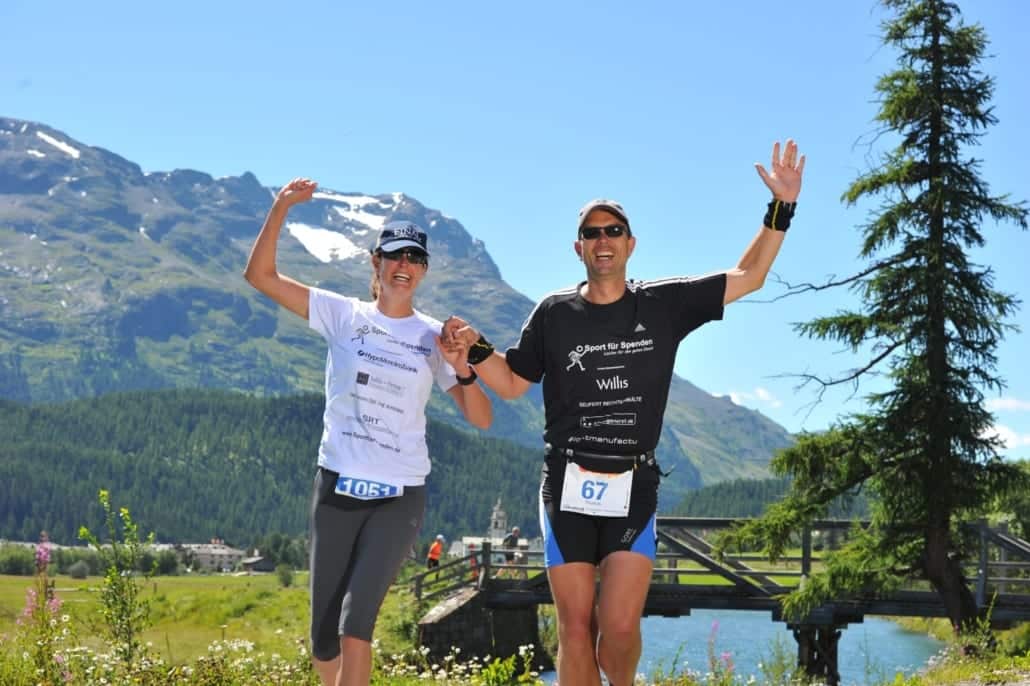 Zwei Läufer in den Alpen im Hintergrund die Berge und ein Fluss.
